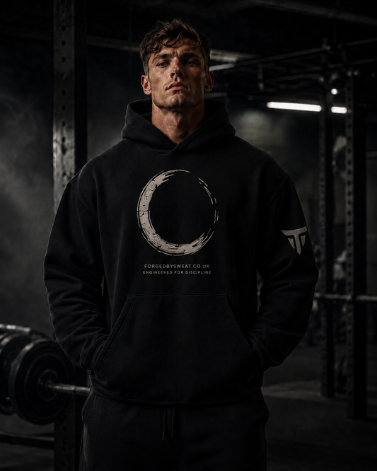 A man wearing a black pullover hoodie with a large circular brushstroke graphic and the text 'FORGEDBYSHIRT.CO.